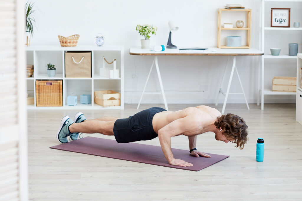 Healthy shirtless man doing push-ups on exercise mat during sports training at home