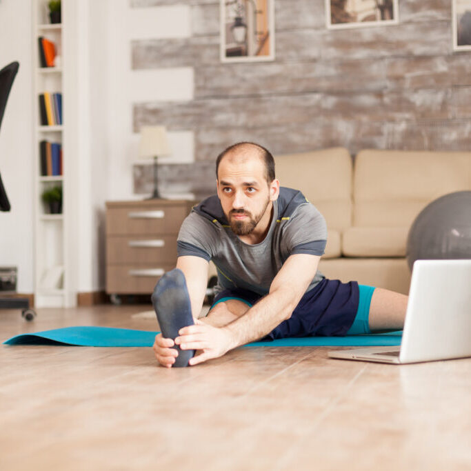 Man doing legs stretching on yoga mat from online training during global lockdown.